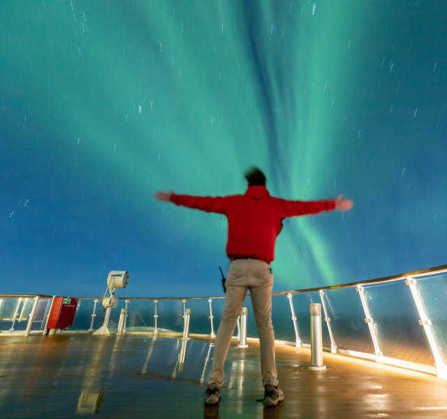 Passenger marvelling at the Northern Lights from the deck of the Greg Mortimer ship in Greenland