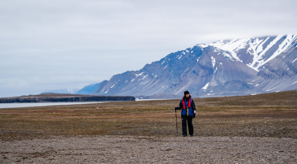 Woman hiking across rocky landscape with mountains, Belsund, Svalbard, Lina Stock @DivergentTravelers